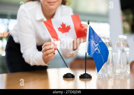 Die Sekretärin setzt die Flaggen der NATO (OTAN) und Kanadas auf den Tisch, bevor Verhandlungen mit hochrangigen politischen Persönlichkeiten geführt werden Stockfoto