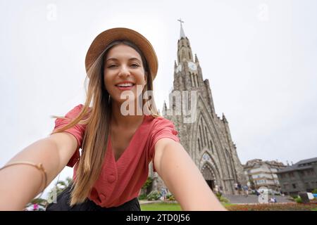 Selfie stylisches Mädchen in Canela, Brasilien. Junge Frau, die Selbstporträt mit der Kirche 'Catedral de Pedra', Canela, Rio Grande do Sul, Brasilien. Stockfoto