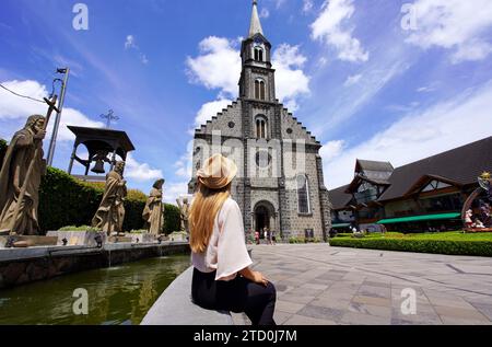 Junge stilvolle Touristenfrau mit Hut auf der Wand, die Gramado Mutterkirche, berühmtes Wahrzeichen und Reiseziel im Bundesstaat Rio Grande do Sul, Stockfoto