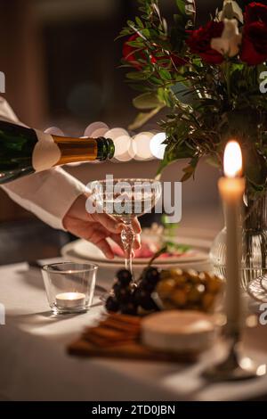 Champagner wird von der Flasche zum Glas auf dem Tisch gegossen Stockfoto