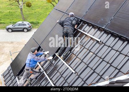 Zwei Techniker arbeiten an der Installation von Solarpaneelen auf dem Dach eines Hauses Stockfoto