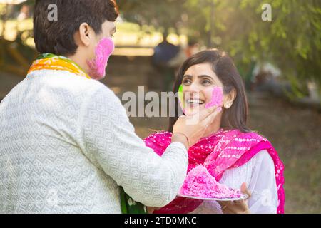 Glückliches, junges indisches Paar, das weiße Kurta spielt und Farbe ins Gesicht bringt. Feiern Sie gemeinsam holi im Freien im Park oder Garten. Stockfoto