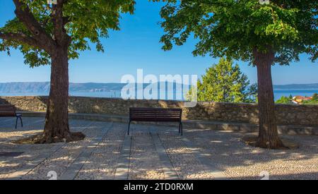 Eine Bank mit Blick auf das Meer im Stari Grad historischen Zentrum von Novi Vinodolski, Komitat Primorje-Gorski Kotar, Kroatien. Krk Island im Hintergrund Stockfoto