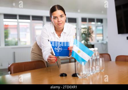 Die junge Dame legt für internationale Verhandlungen Miniaturflaggen von Argentinien und der NATO Stockfoto