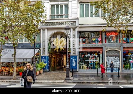 Zwei Frauen und ein Hund überqueren die Straße am Eingang zur Passage Jouffroy am Boulevard Montmartre, einer der beliebtesten überdachten Gänge in Paris Stockfoto