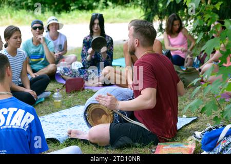 Junger Mann Musiker Mönch spielt indisches Schlaginstrument Mridangam für Meditation, Gruppe von Leuten hört zu. Juli 2020. Kiew, Ukraine Stockfoto