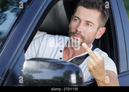 Fahrer Mann im Auto lächelt und zeigt Schild Mittelfinger Stockfoto