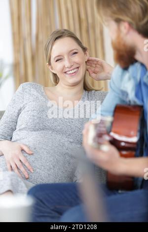 Junger Mann spielt Gitarre für seine schöne schwangere Frau Stockfoto