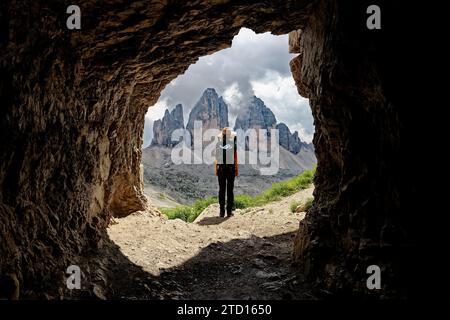 Eine weibliche Person, die den Blick auf den Berg Tre Cime di Lavaredo in den Dolomiten, Italien, bewundert. Berühmte Orte zum Wandern. Blick aus dem Inneren einer Höhle. Stockfoto