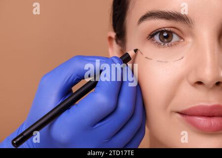 Arzt zeichnet Zeichen auf das Gesicht der Frau für kosmetische Operationen vor beigefarbenem Hintergrund, Nahaufnahme Stockfoto