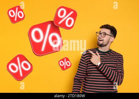 Rabattangebot. Glücklicher Mann, der auf fallende Würfel zeigt, mit Prozentzeichen auf orangem Hintergrund Stockfoto