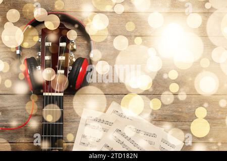 Weihnachtsmusik und Neujahrsmusik. Kopfhörer, Gitarre und Notenblätter auf hölzernem Hintergrund, Bokeh-Effekt Stockfoto