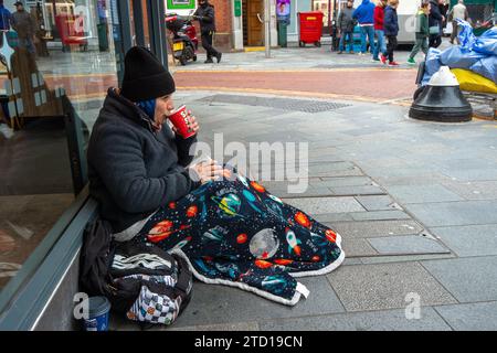 Maidenhead, Großbritannien. Dezember 2023. Eine Frau bittet um Geld vor einer Greggs-Bäckerei in Maidenhead, Berkshire, die im Wahlkreis der ehemaligen Premierministerin Theresa May liegt. Polly Neate, Chief Executive von Shelter, sagte Sky News, dass Obdachlosigkeit auf der Weihnachtsliste von niemandem steht, aber 309.000 Menschen werden diese Zeit des Jahres in einem winzigen Hostel-Zimmer verbringen oder in einer Tür frieren. Quelle: Maureen McLean/Alamy Live News Stockfoto