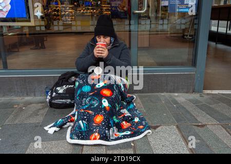 Maidenhead, Großbritannien. Dezember 2023. Eine Frau bittet um Geld vor einer Greggs-Bäckerei in Maidenhead, Berkshire, die im Wahlkreis der ehemaligen Premierministerin Theresa May liegt. Polly Neate, Chief Executive von Shelter, sagte Sky News, dass Obdachlosigkeit auf der Weihnachtsliste von niemandem steht, aber 309.000 Menschen werden diese Zeit des Jahres in einem winzigen Hostel-Zimmer verbringen oder in einer Tür frieren. Quelle: Maureen McLean/Alamy Live News Stockfoto