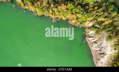 Dieses Bild ist aus der Luftperspektive aufgenommen und erfasst die anmutige Kurve eines Flusses, der sich durch eine üppige Landschaft schlängelt. Das lebhafte grüne Wasser steht in starkem Kontrast zum felsigen Damm auf der einen Seite, wo Erosion Muster sichtbar sind, die die dynamischen Kräfte der Natur im Spiel zeigen. Das gegenüberliegende Ufer ist mit einem Wandteppich von Bäumen in verschiedenen Herbsttönen gesäumt, deren Laub auf die wechselnden Jahreszeiten hindeutet. Die Komposition hebt die Schnittmenge von Wasser, Erde und Leben hervor und zeigt die vielfältigen Texturen und Farben der natürlichen Welt. Blick aus der Vogelperspektive auf eine grüne Flussbiegung mit Roc Stockfoto