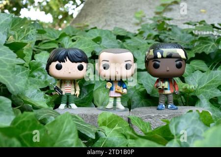 Funko Pop Actionfiguren von Mike, Eleven und Lucas aus der Netflix Supernatural TV-Serie Stranger Things. Grüne Efeublätter, verlassener Garten. Stockfoto