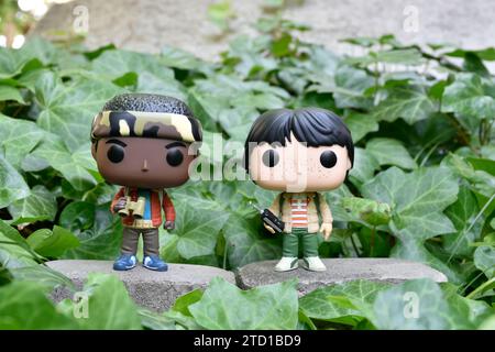 Funko Pop Actionfiguren von Lucas und Mike aus der Netflix TV-Serie Stranger Things. Grüne Efeupflanzen, verlassener Garten, Abenteuer, Freundschaft. Stockfoto