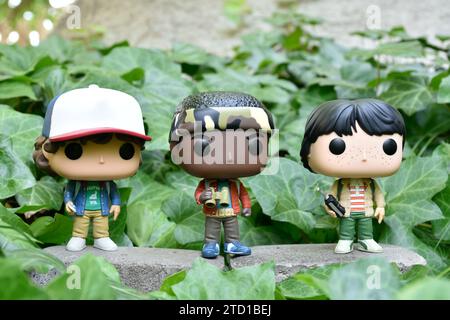 Funko Pop Actionfiguren von Dustin, Lucas und Mike aus der Netflix TV-Serie Stranger Things. Grüne Efeublätter, verlassener Garten. Stockfoto