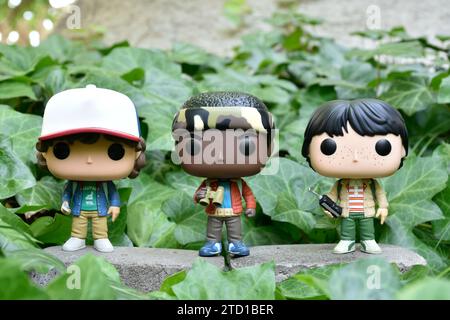 Funko Pop Actionfiguren von Dustin, Lucas und Mike aus der Netflix TV-Serie Stranger Things. Grüne Efeublätter, verlassener Garten. Stockfoto