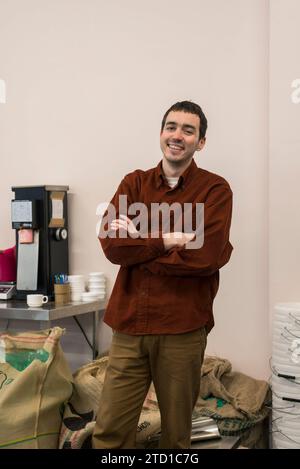 Ein männlicher Geschäftsinhaber steht vor Kaffeemühle, wo er Spezialkaffee für den Verkauf herstellt. Stockfoto