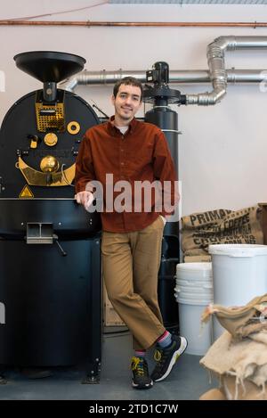 Ein männlicher Geschäftsinhaber steht vor Kaffeemühle, wo er Spezialkaffee für den Verkauf herstellt. Stockfoto