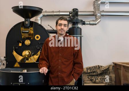 Ein männlicher Geschäftsinhaber steht vor Kaffeemühle, wo er Spezialkaffee für den Verkauf herstellt. Stockfoto