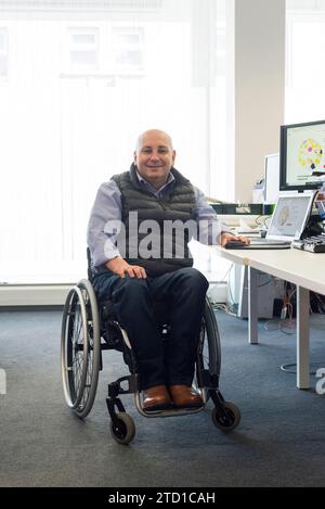 Ein Mann im Rollstuhl ist in seinem IT-Technikbüro, das einen guten Zugang für Behinderte hat Stockfoto