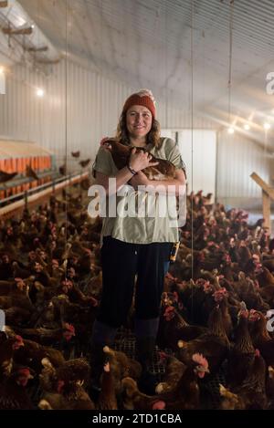 Eine Farmerin hält ein Huhn, umgeben von Hühnern und Hühnern. Stockfoto
