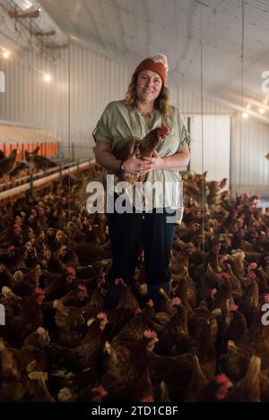Eine Farmerin hält ein Huhn, umgeben von Hühnern und Hühnern. Stockfoto