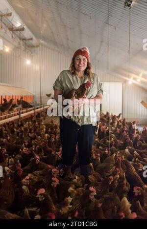 Eine Farmerin hält ein Huhn, umgeben von Hühnern und Hühnern. Stockfoto