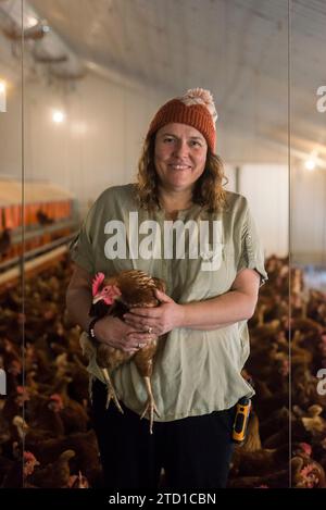 Eine Farmerin hält ein Huhn, umgeben von Hühnern und Hühnern. Stockfoto