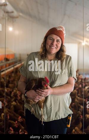 Eine Farmerin hält ein Huhn, umgeben von Hühnern und Hühnern. Stockfoto