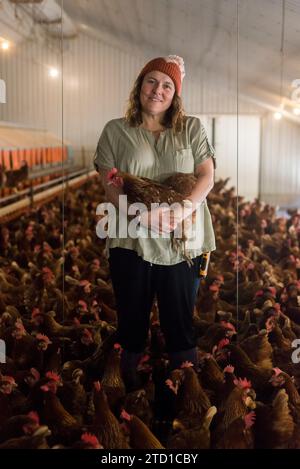 Eine Farmerin hält ein Huhn, umgeben von Hühnern und Hühnern. Stockfoto