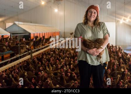 Eine Farmerin hält ein Huhn, umgeben von Hühnern und Hühnern. Stockfoto