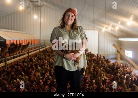 Eine Farmerin hält ein Huhn, umgeben von Hühnern und Hühnern. Stockfoto
