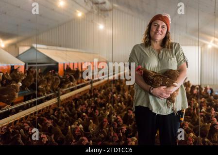 Eine Farmerin hält ein Huhn, umgeben von Hühnern und Hühnern. Stockfoto