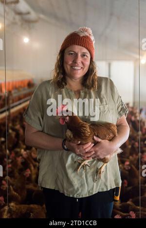 Eine Farmerin hält ein Huhn, umgeben von Hühnern und Hühnern. Stockfoto