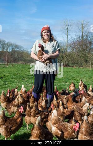 Eine Farmerin hält ein Huhn, umgeben von Hühnern und Hühnern. Stockfoto