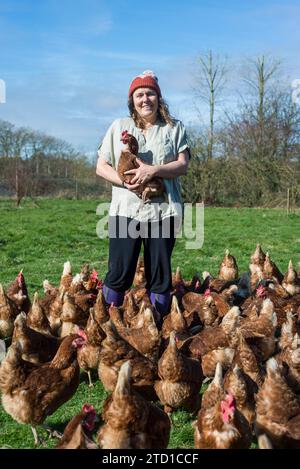 Eine Farmerin hält ein Huhn, umgeben von Hühnern und Hühnern. Stockfoto