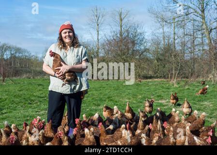 Eine Farmerin hält ein Huhn, umgeben von Hühnern und Hühnern. Stockfoto