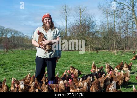 Eine Farmerin hält ein Huhn, umgeben von Hühnern und Hühnern. Stockfoto