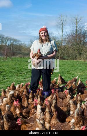 Eine Farmerin hält ein Huhn, umgeben von Hühnern und Hühnern. Stockfoto