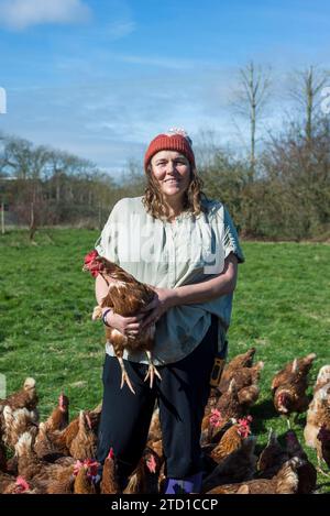 Eine Farmerin hält ein Huhn, umgeben von Hühnern und Hühnern. Stockfoto