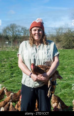 Eine Farmerin hält ein Huhn, umgeben von Hühnern und Hühnern. Stockfoto