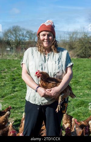 Eine Farmerin hält ein Huhn, umgeben von Hühnern und Hühnern. Stockfoto