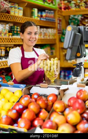 Positive junge Frau, die einen Haufen reifer Trauben hält und frisches Obst anbietet und in die Kamera schaut Stockfoto