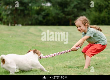 Kind und Hund spielen am Spielzeugseil auf dem Garten Stockfoto