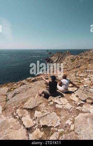 Zwei Frauen sitzen auf den Felsen, um eine Pause von der Wanderung nach Pointe du Raz in der Bretagne zu machen Stockfoto