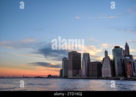 Blick auf das Finanzviertel von Manhattan und die Freiheitsstatue vom Brooklyn Bridge Park in der Abenddämmerung - New York City, USA Stockfoto