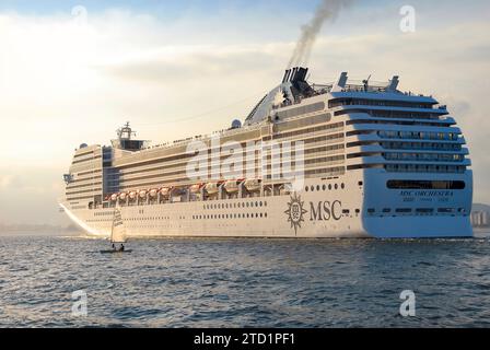 Kreuzfahrtschiff MSC Orchestra Segeln bei Sonnenuntergang. Segelboot neben dem Schiff. Stadtgebäude im Hintergrund. Santos City, Brasilien. Stockfoto